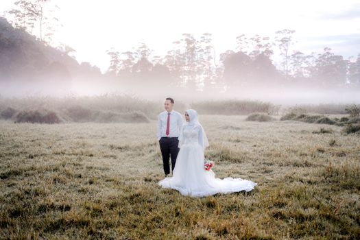 Beautiful wedding couple posing in a misty field, showcasing love and elegance. - Fotografer Sidoarjo