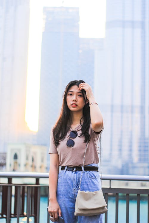 Kostnadsfri bild av asiatisk kvinna, brun skjorta, handen på håret