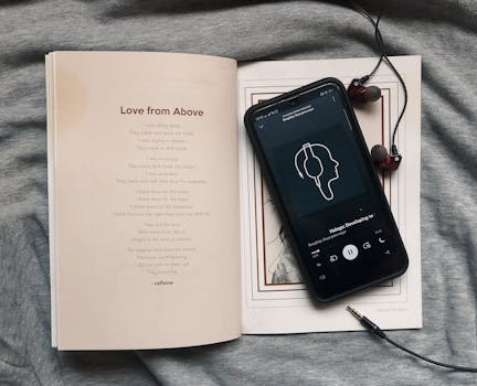 Smartphone playing music with earphones on an open book.
