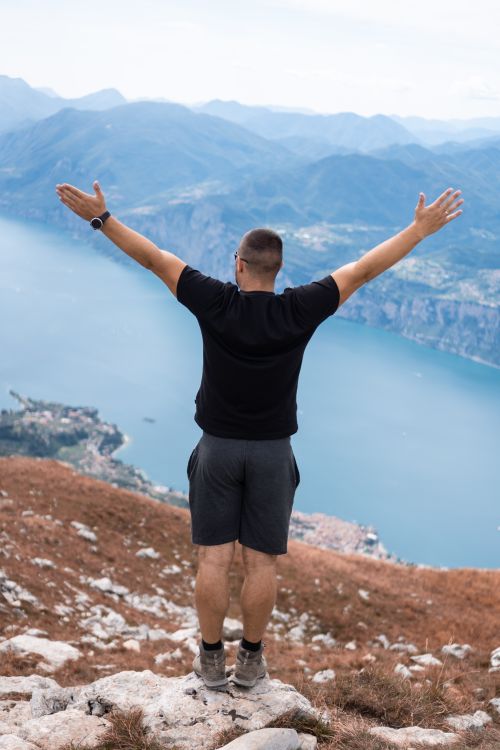 Free A man stands with arms raised atop a mountain, embracing the freedom and beauty of nature. Stock Photo