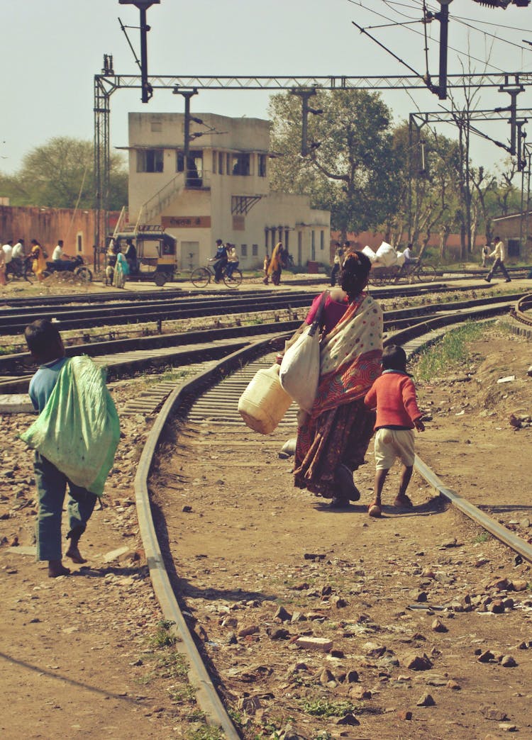 Mother And Two Sons Carrying Bags Along Railway Tracks