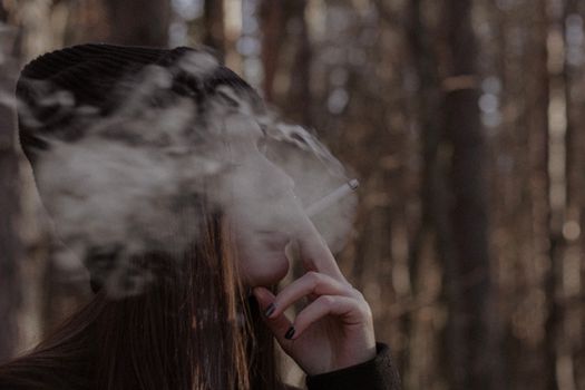 Woman smoking in a forest, with focused side view and blurred background.