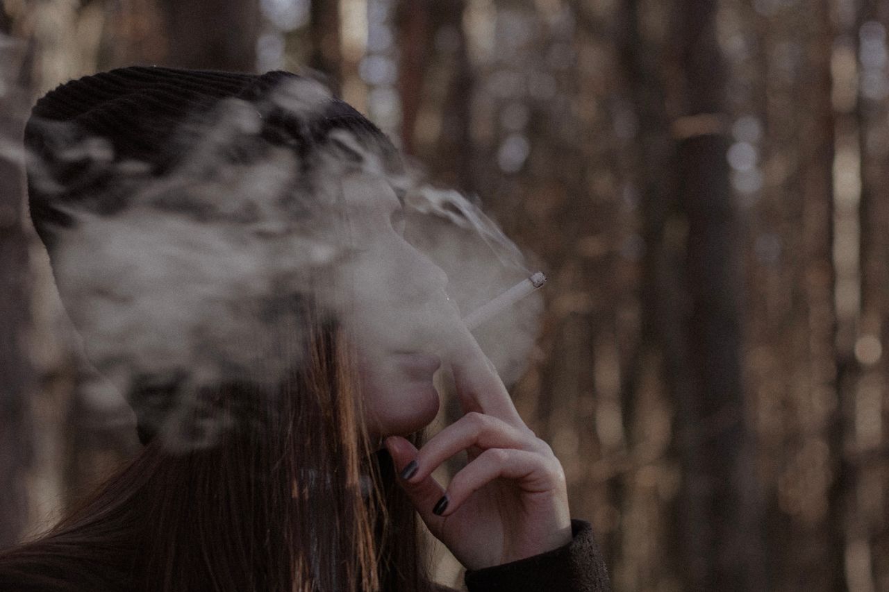 woman smoking in a forest with focused side view and blurred backgroun