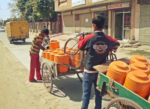 Two Men Transporting Orange Colored Barrels on Rickshaw Carts