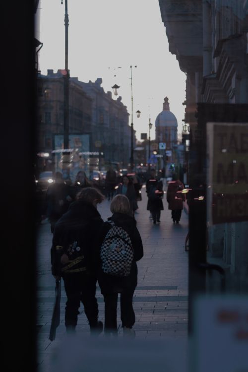 Free Two people walking in a vibrant city street at dusk with streetlights illuminating the path. Stock Photo