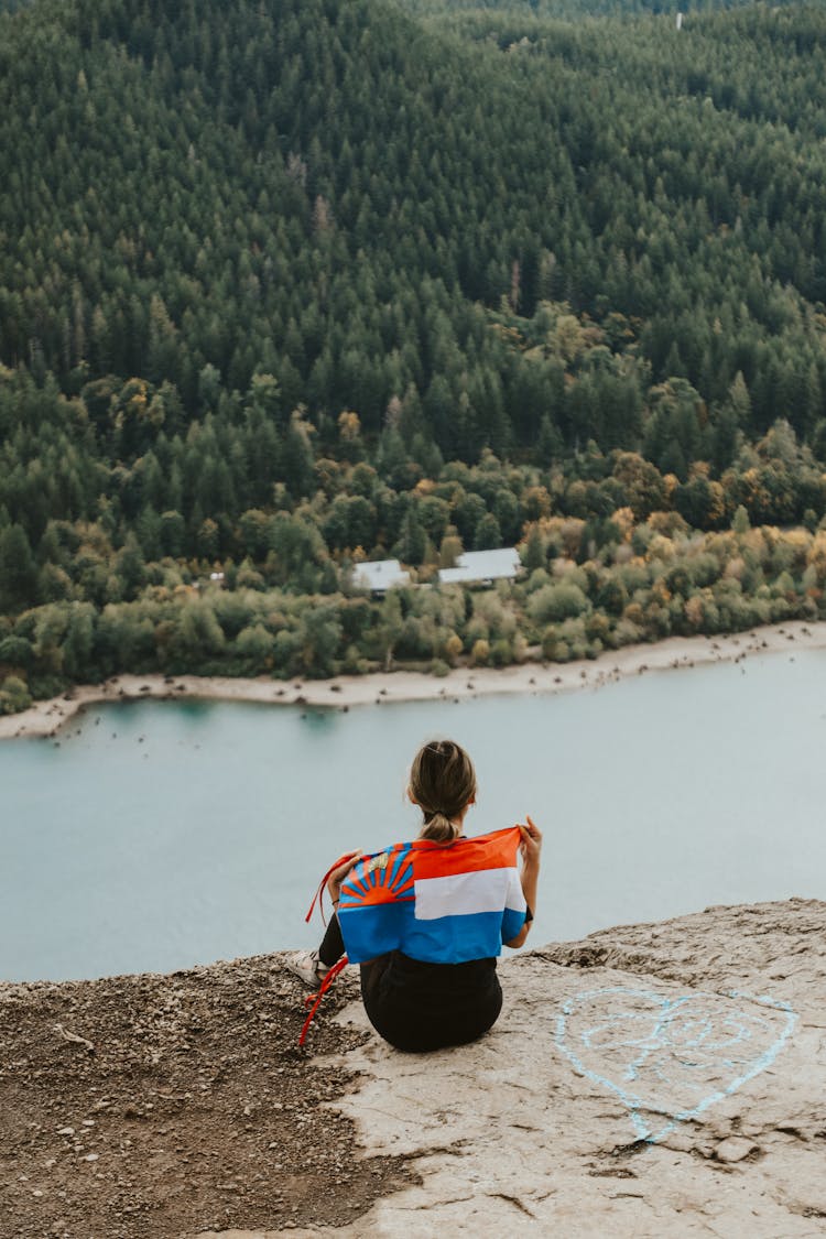 Woman Sitting At The Edge Of A Lakeshore Cliff