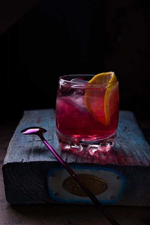 Free Close-up of a vibrant red cocktail in a glass with lemon slice on rustic wood. Stock Photo