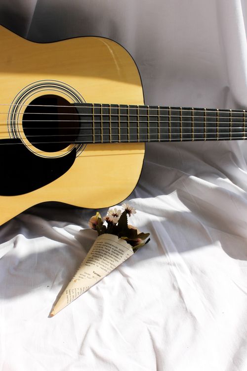 Free Close-up view of an acoustic guitar with a small bouquet on white fabric. Ideal for music and lifestyle themes. Stock Photo