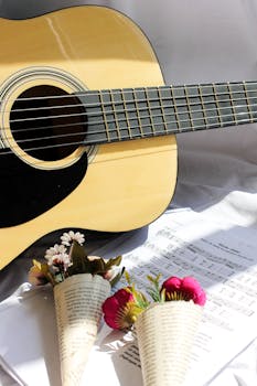 An acoustic guitar alongside sheet music and floral bouquets in natural light.