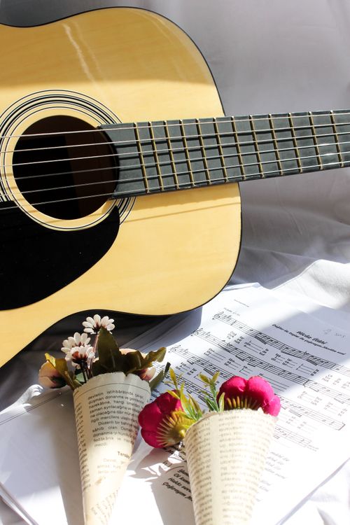 Free An acoustic guitar alongside sheet music and floral bouquets in natural light. Stock Photo