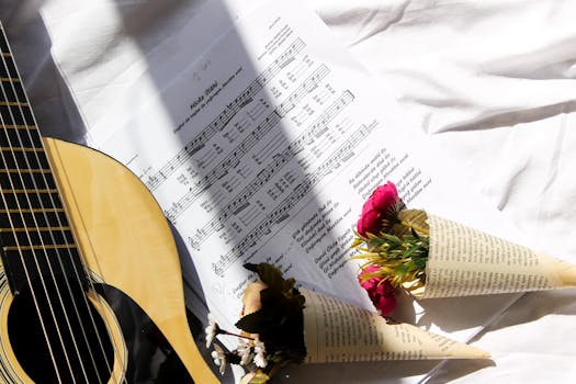 Acoustic guitar with sheet music and flower bouquets on white fabric surface.