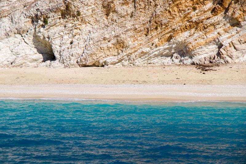 Beautiful turquoise waters meeting a sandy beach beneath rugged cliffs in Greece