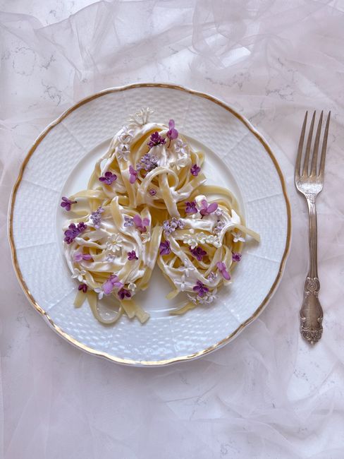 Elegant pasta dish garnished with edible flowers on a white plate, perfect for gourmet dining concepts.