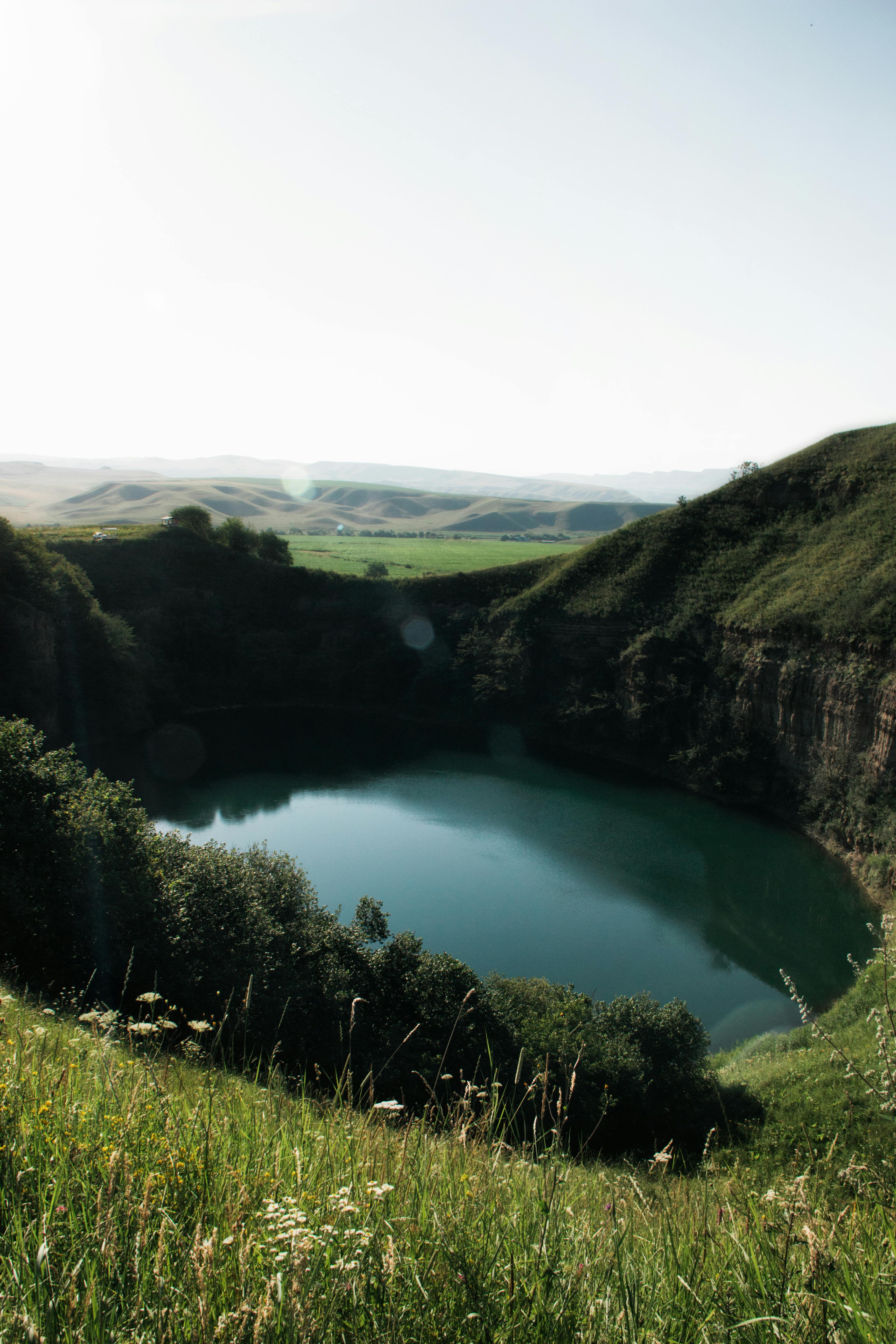 A breathtaking high angle view of a tranquil lake surrounded by lush green hills and distant rolling mountains.