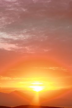 Capture the serene beauty of a golden sunset streaming over mountain peaks and vibrant clouds.