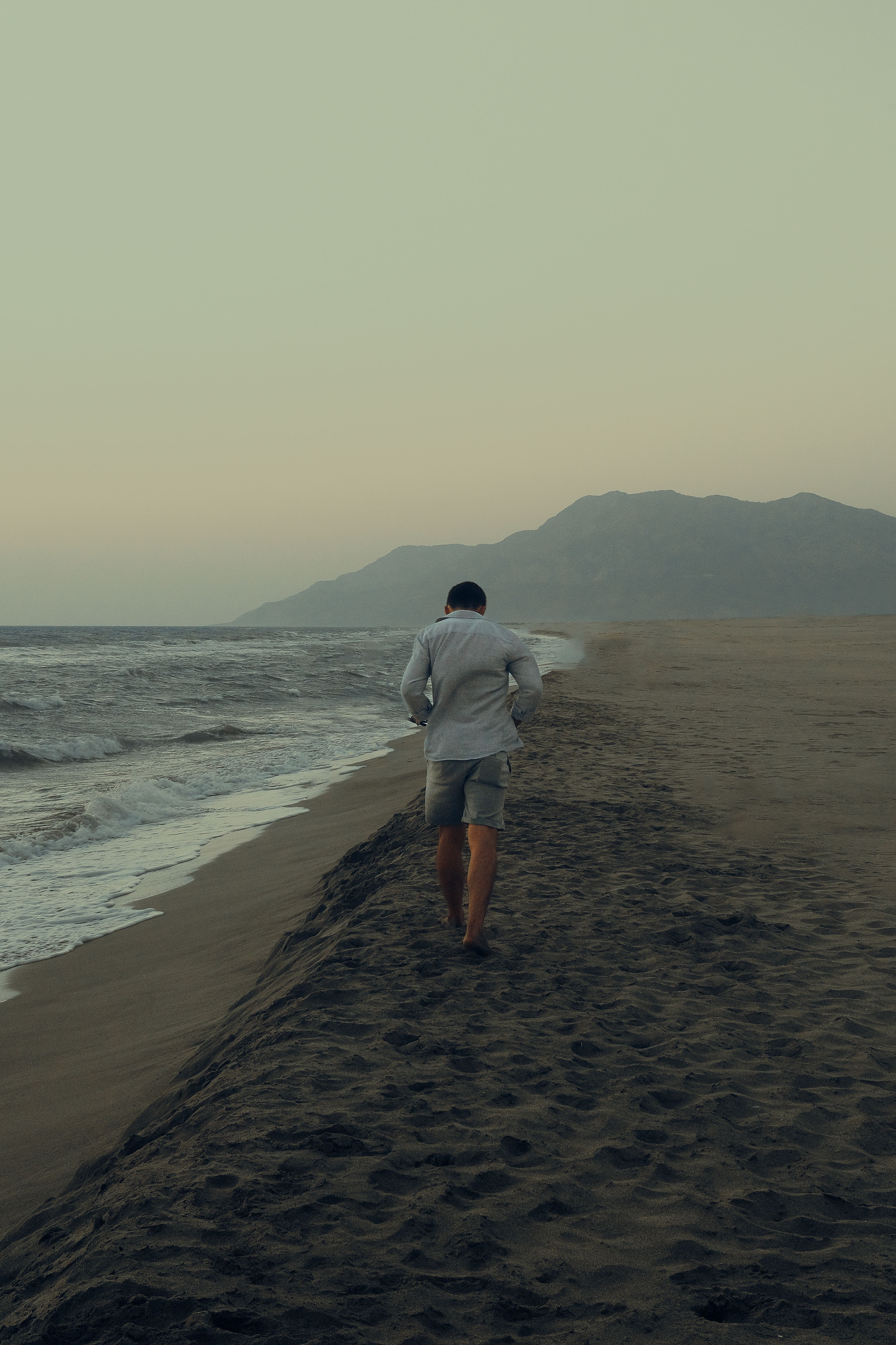 Person walking on a beach path with mountains in the distance