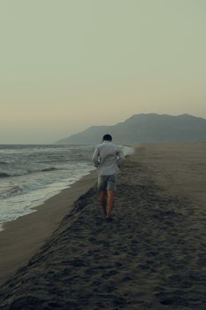 Man walking alone on a quiet beach with mountains in the background at twilight.