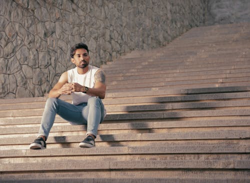 Man in White Muscle Shirt and Blue Denim Jeans Sitting on Stairs