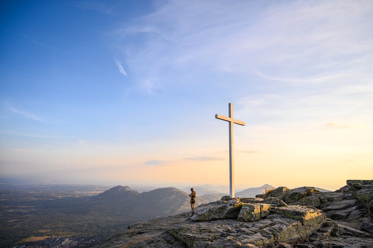 Person Standing Near A Cross On Top Of A Mountain