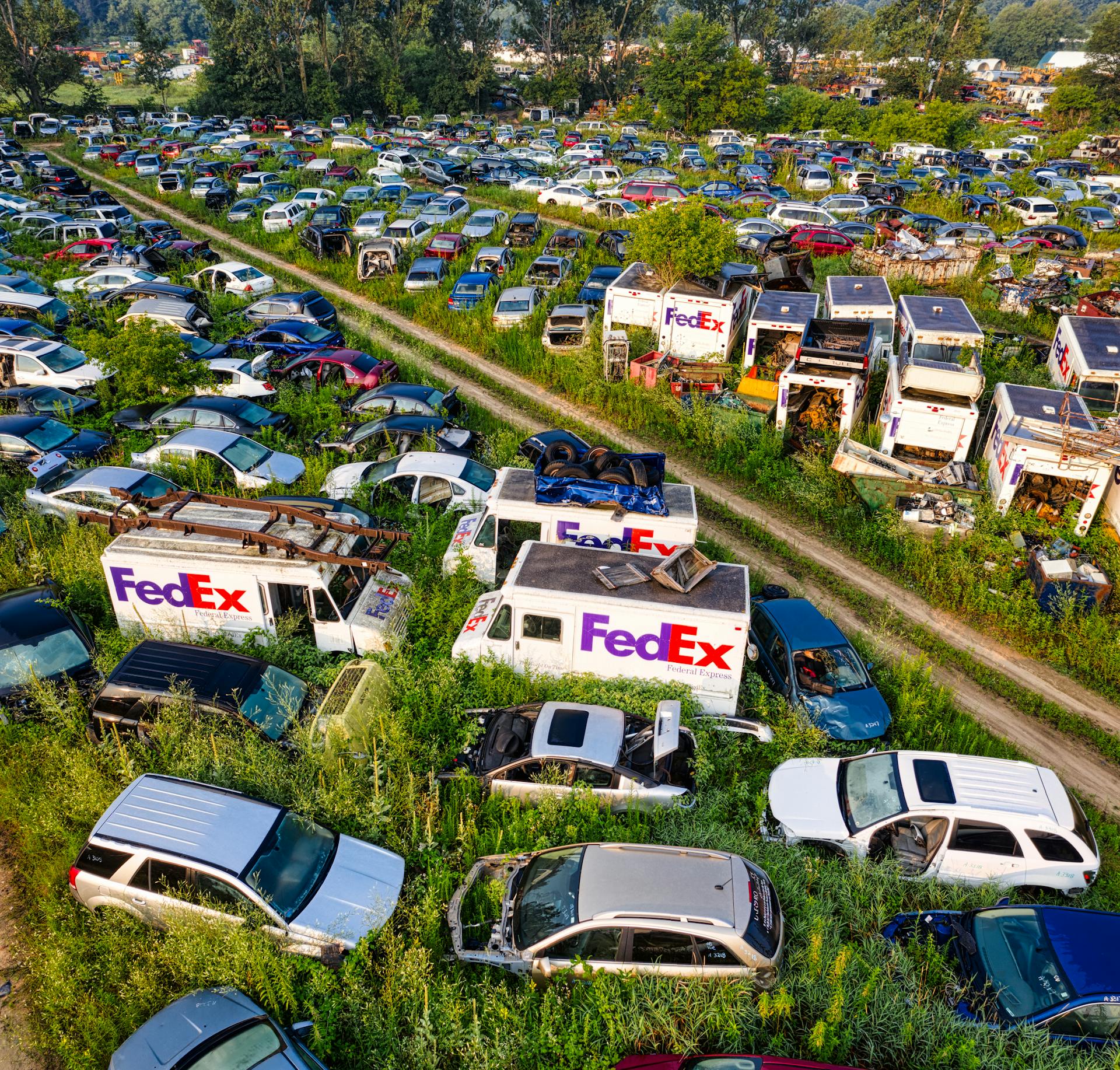 Aerial shot of multiple abandoned FedEx trucks and vehicles on a rural dirt road in Saint Charles, MN.