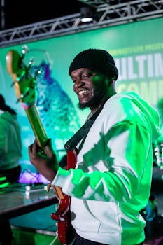 African American bassist wearing a beanie performs passionately on stage during a vibrant night concert.