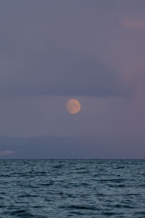 Free Peaceful ocean scene with a full moon rising above calm waters, captured under a twilight sky. Stock Photo
