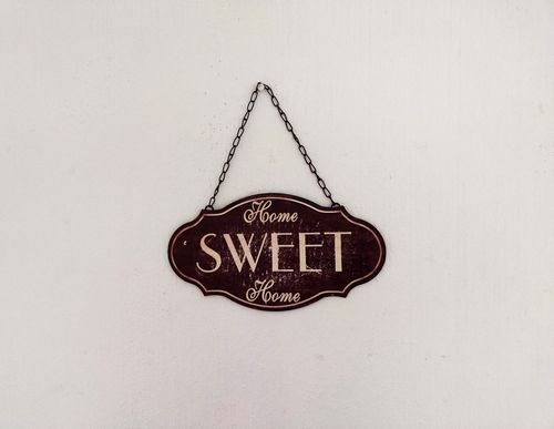 Free A close-up of a vintage 'Home Sweet Home' sign hanging on a white wall. Stock Photo