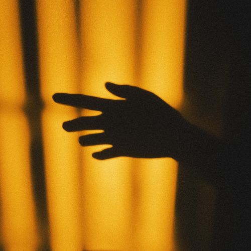 Free Artistic shadow silhouette of a hand against a warm golden background. Stock Photo