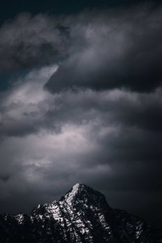 A striking snowcapped mountain peak beneath a dramatic and cloud-filled sky, conveying a sense of adventure and nature's raw beauty.