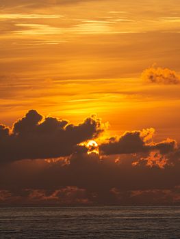 Stunning sunset scene with the sun setting behind clouds and reflecting on the ocean.