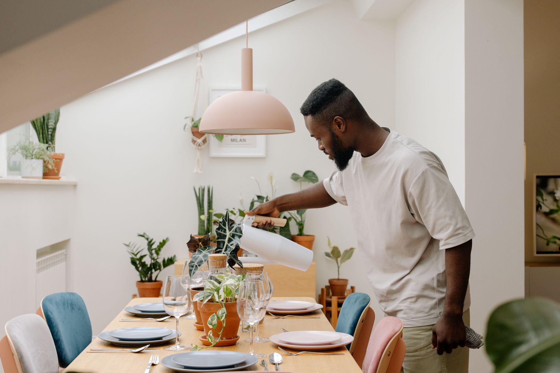 A man waters stylish houseplants in a cozy dining room setting with a modern aesthetic.