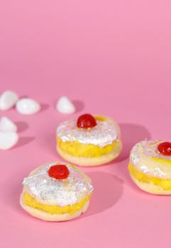 Three sweet pastries topped with icing and cherries on a pink background.