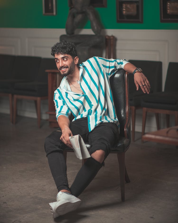 Man In Striped Polo Shirt And Black Ripped Jeans Sitting On Black Leather Chair