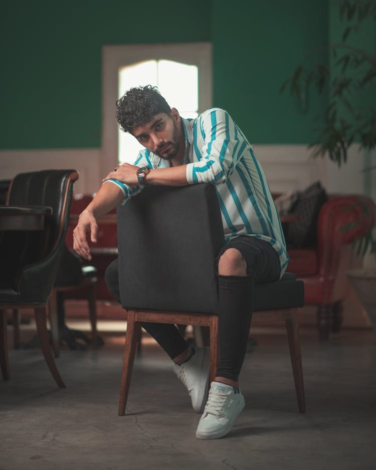 Man In Striped Shirt And Ripped Jeans Sitting On Black Chair