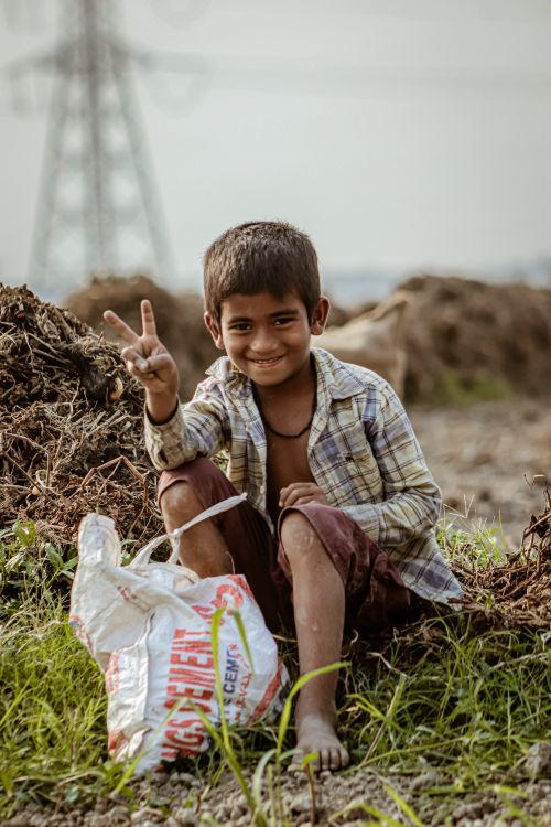 Free Smiling young boy sitting outdoors showing peace sign with a friendly expression. Stock Photo