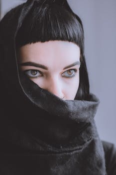 Close-up of a mysterious woman with striking eyes wrapped in dark fabric, exuding intrigue.
