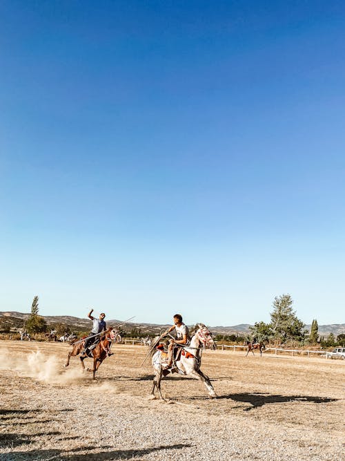 People Riding Horses on Brown Field Under Blue Sky