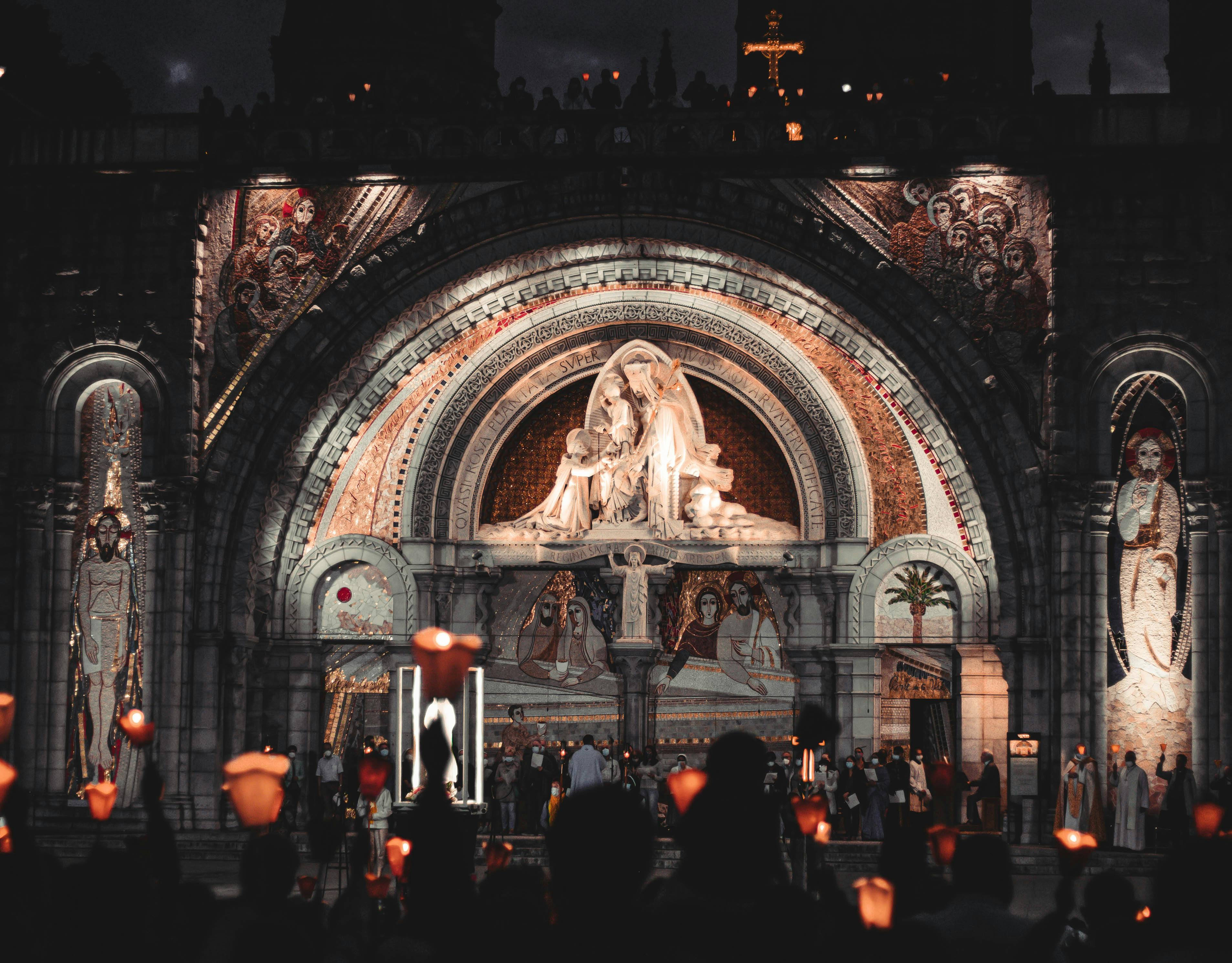 Beautiful nighttime vigil at Lourdes, France, with glowing candles and statues.