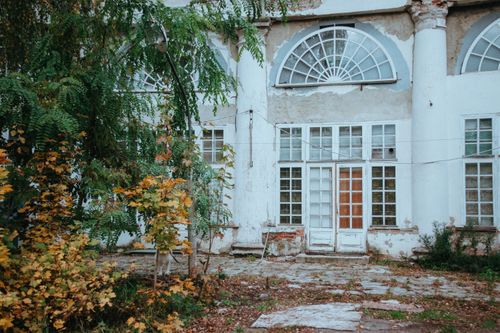 Free A deserted, weathered building with arched glass windows, overgrown with lush ivy and autumn foliage. Stock Photo