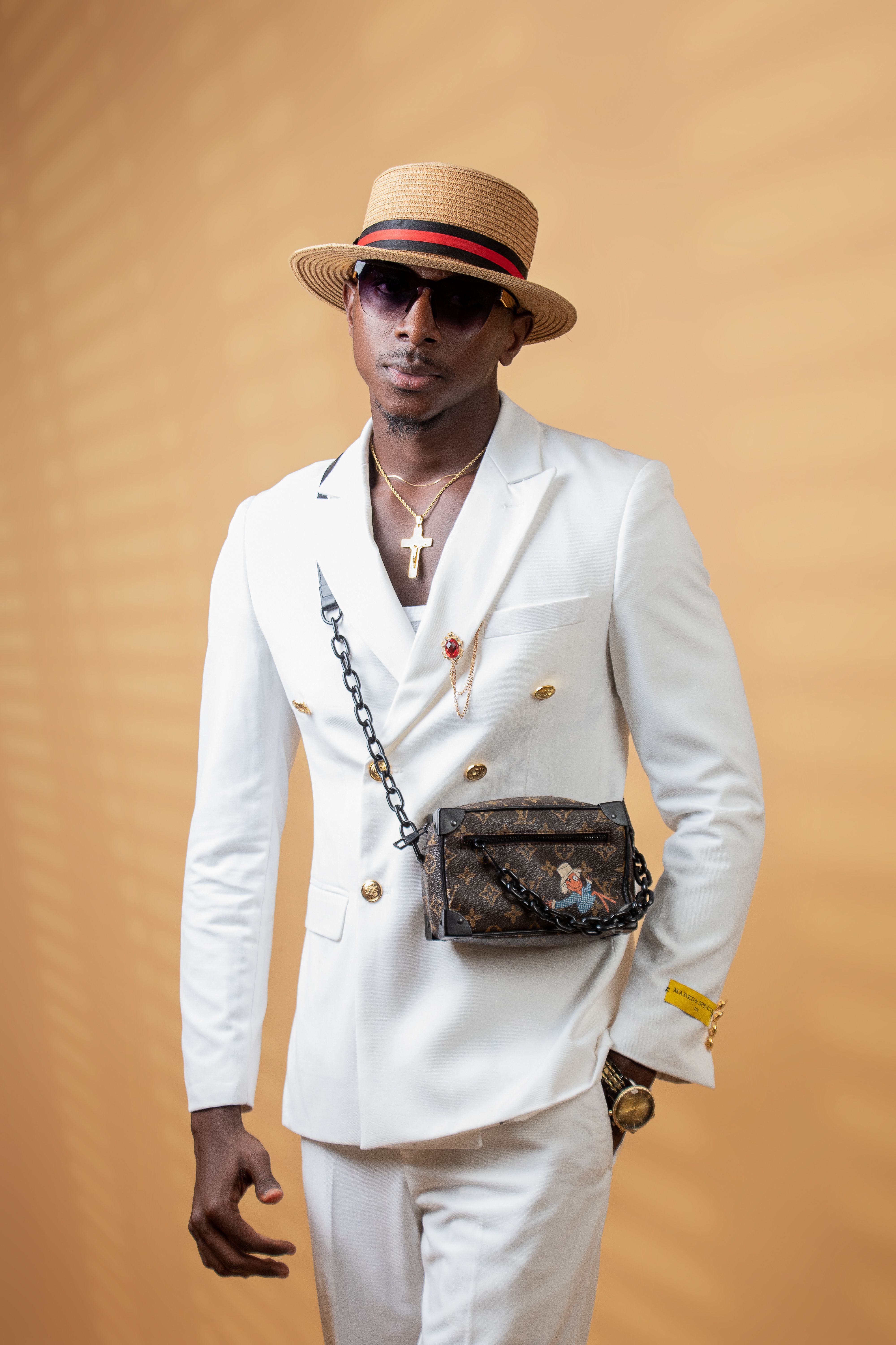 Chic African American man in white suit and stylish accessories against a warm background.