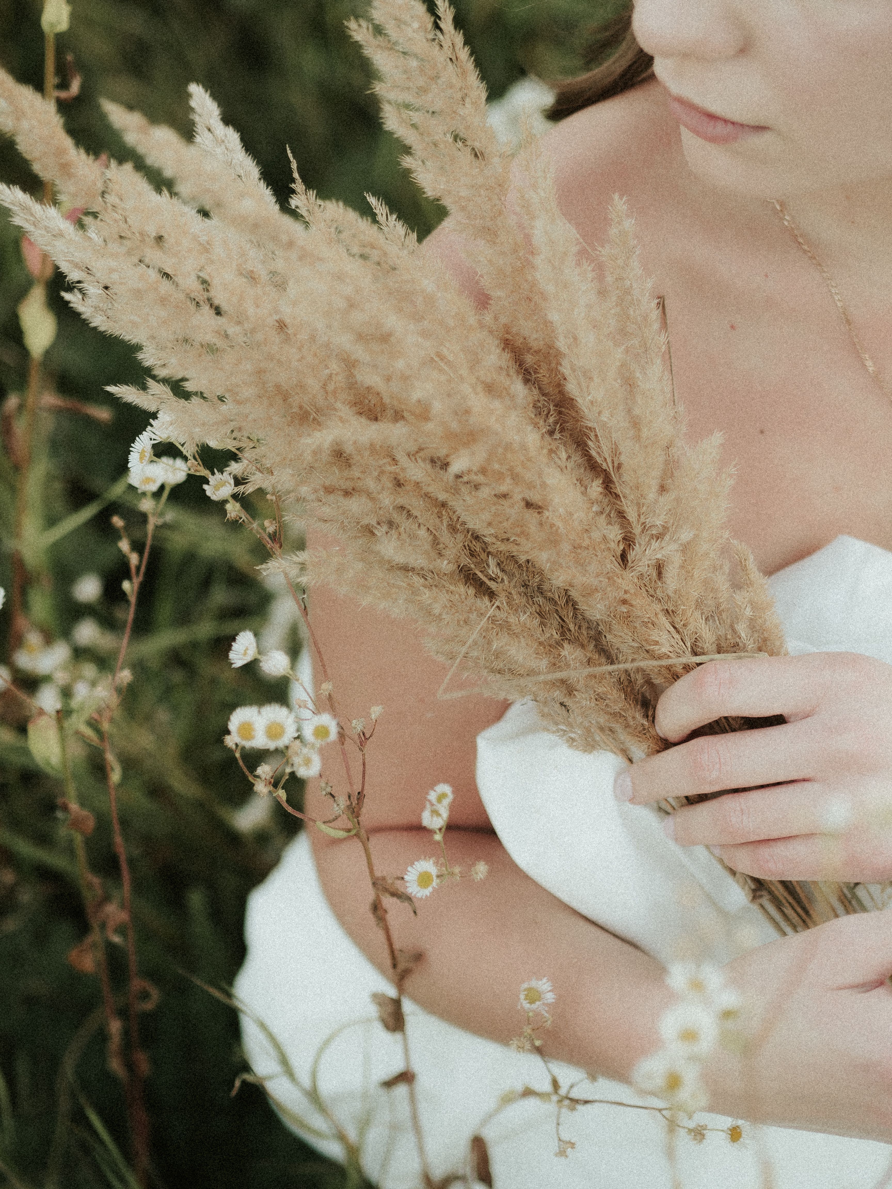 A serene portrait featuring a woman holding pampas grass amidst white daisies in a green field.