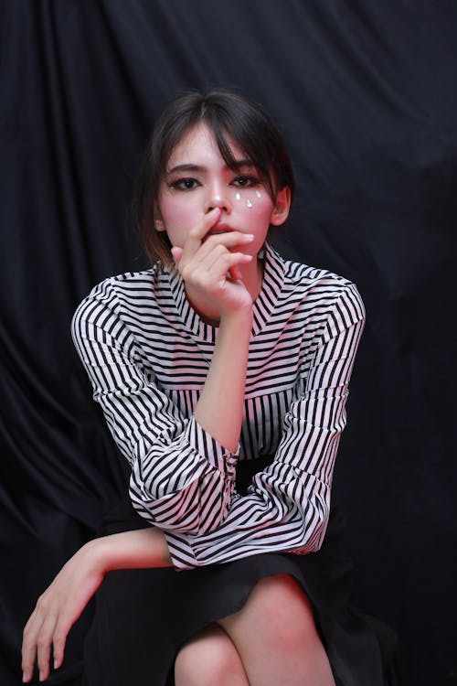 Free Woman in Black and White Stripe Long Sleeves Shirt Sitting while Seriously Looking at the Camera Stock Photo