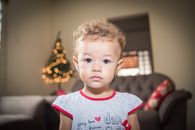 一个可爱的卷发幼儿站在室内，背景是模糊的节日灯光