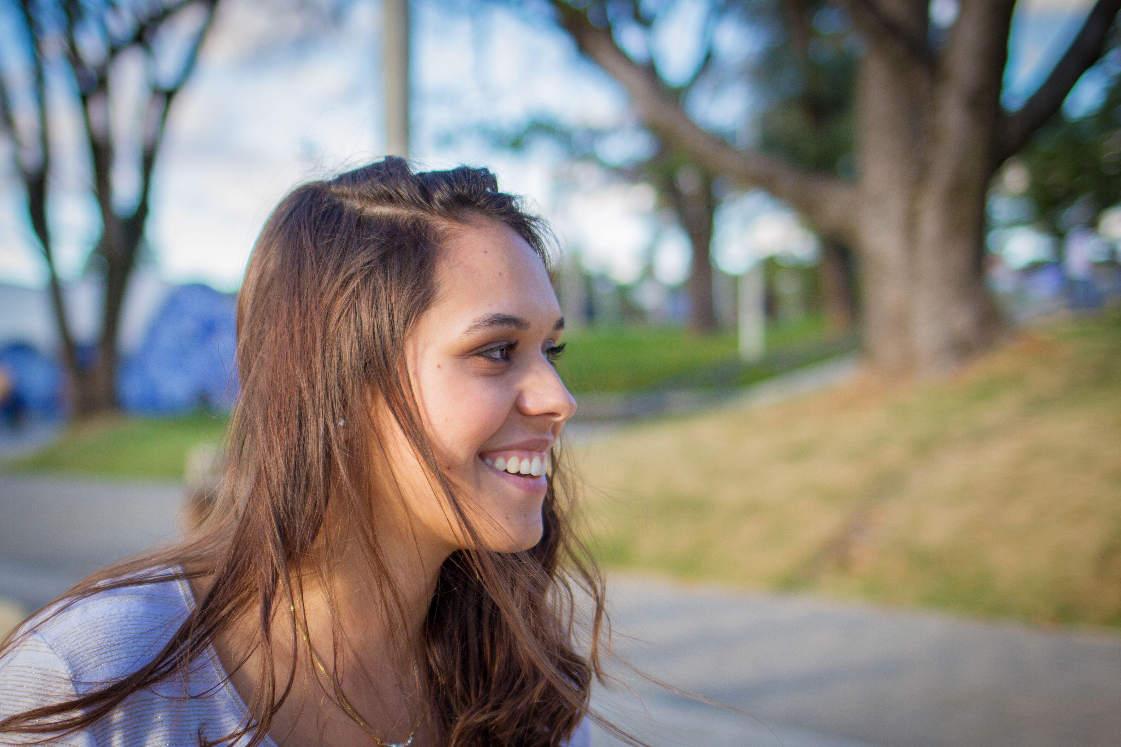 Happy young woman smiling under the bright daylight in a park setting.