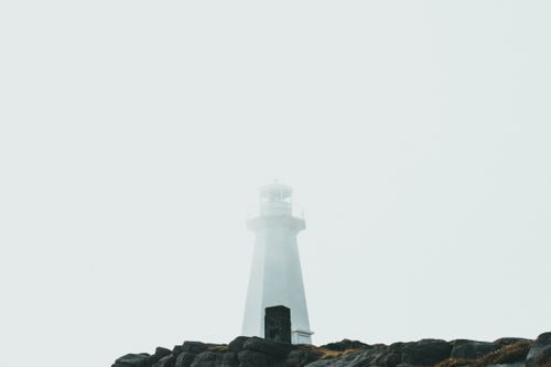 Free Misty view of a lighthouse emerging from the fog on a rocky coastline, symbolizing guidance and safety. Stock Photo