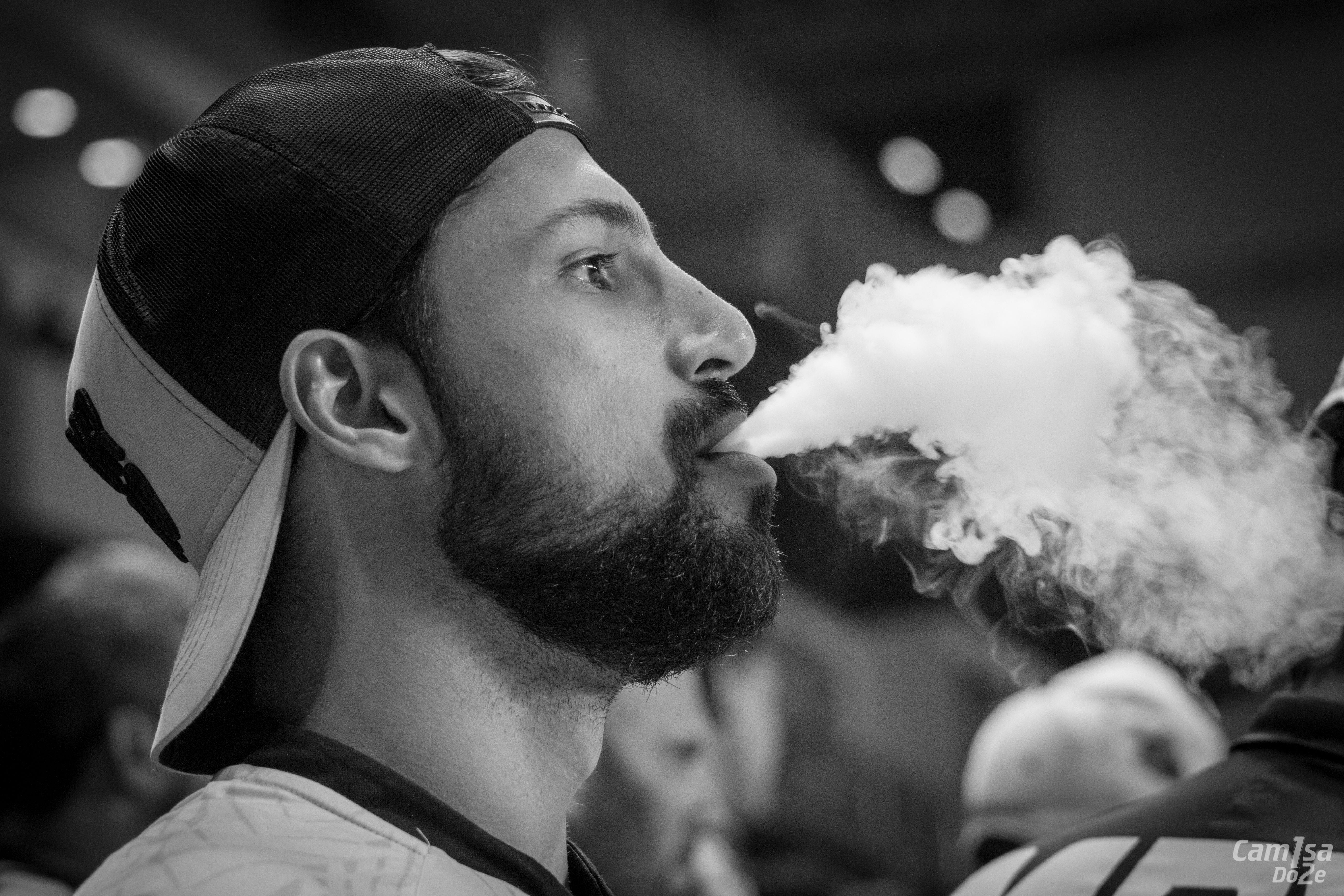 grayscale photography of man wearing cap with smoke on mouth