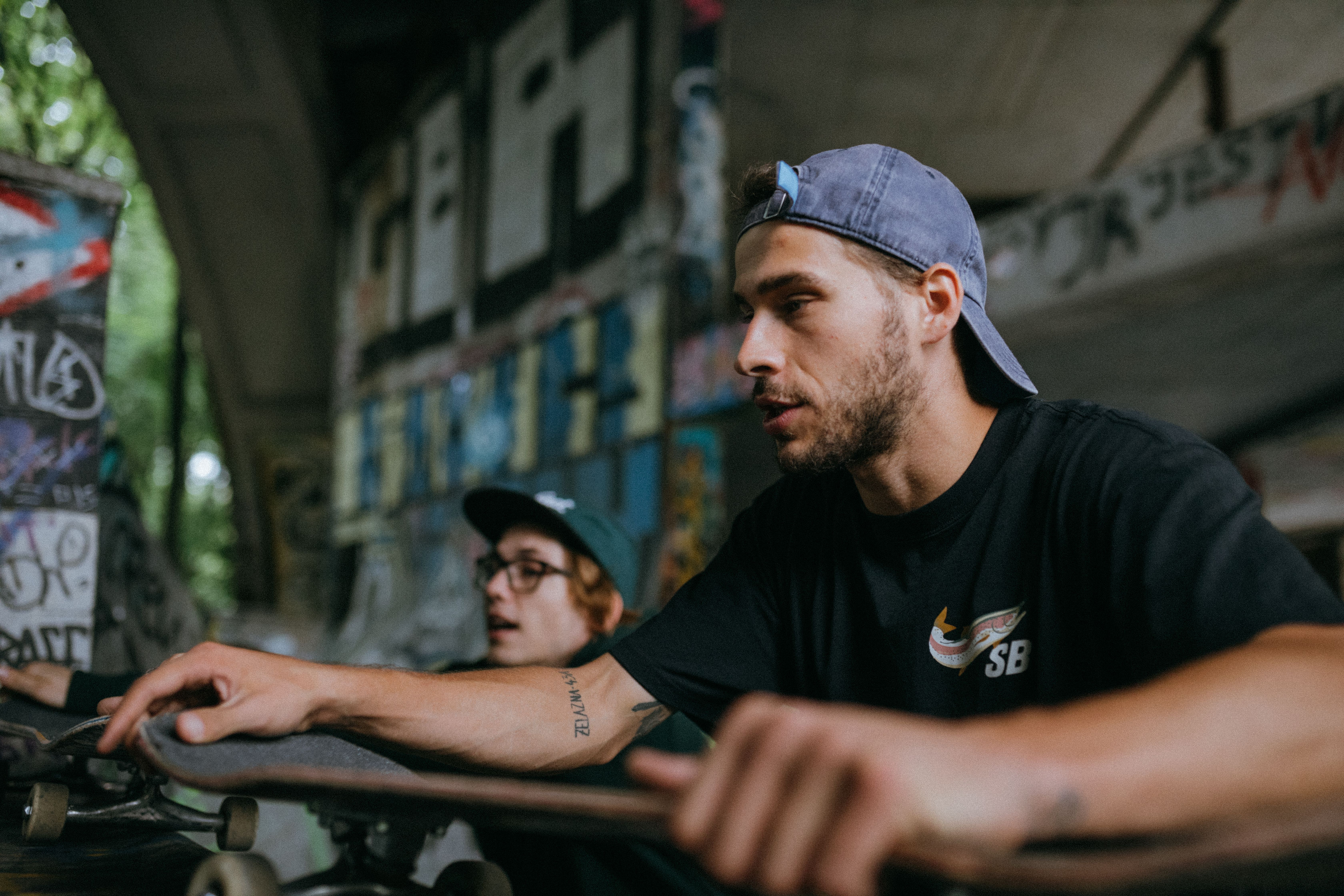 Two men with skateboards under a graffiti tunnel, highlighting urban lifestyle and youth culture.