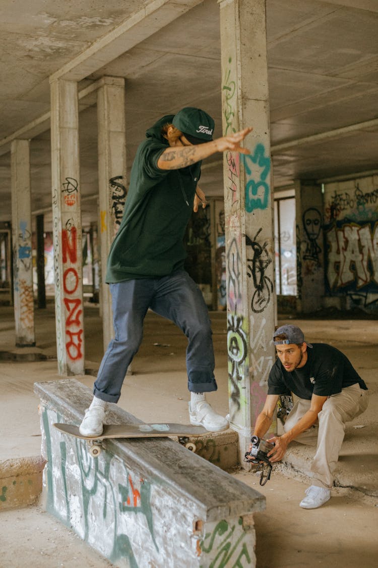 Man Filming Another Man Doing Tricks On Skateboard