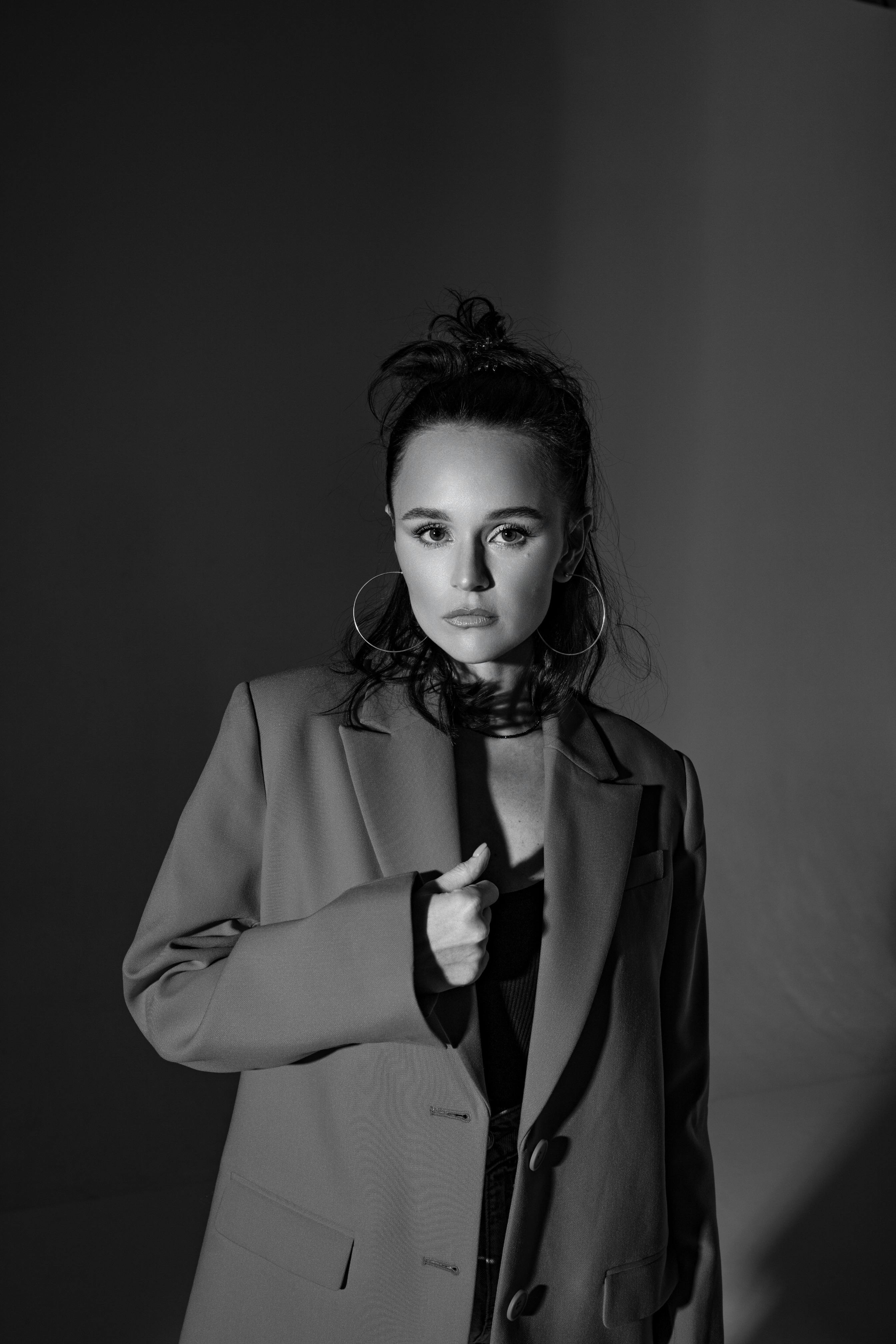 Stylish black and white portrait of a young woman in a tailored jacket with bold jewelry.