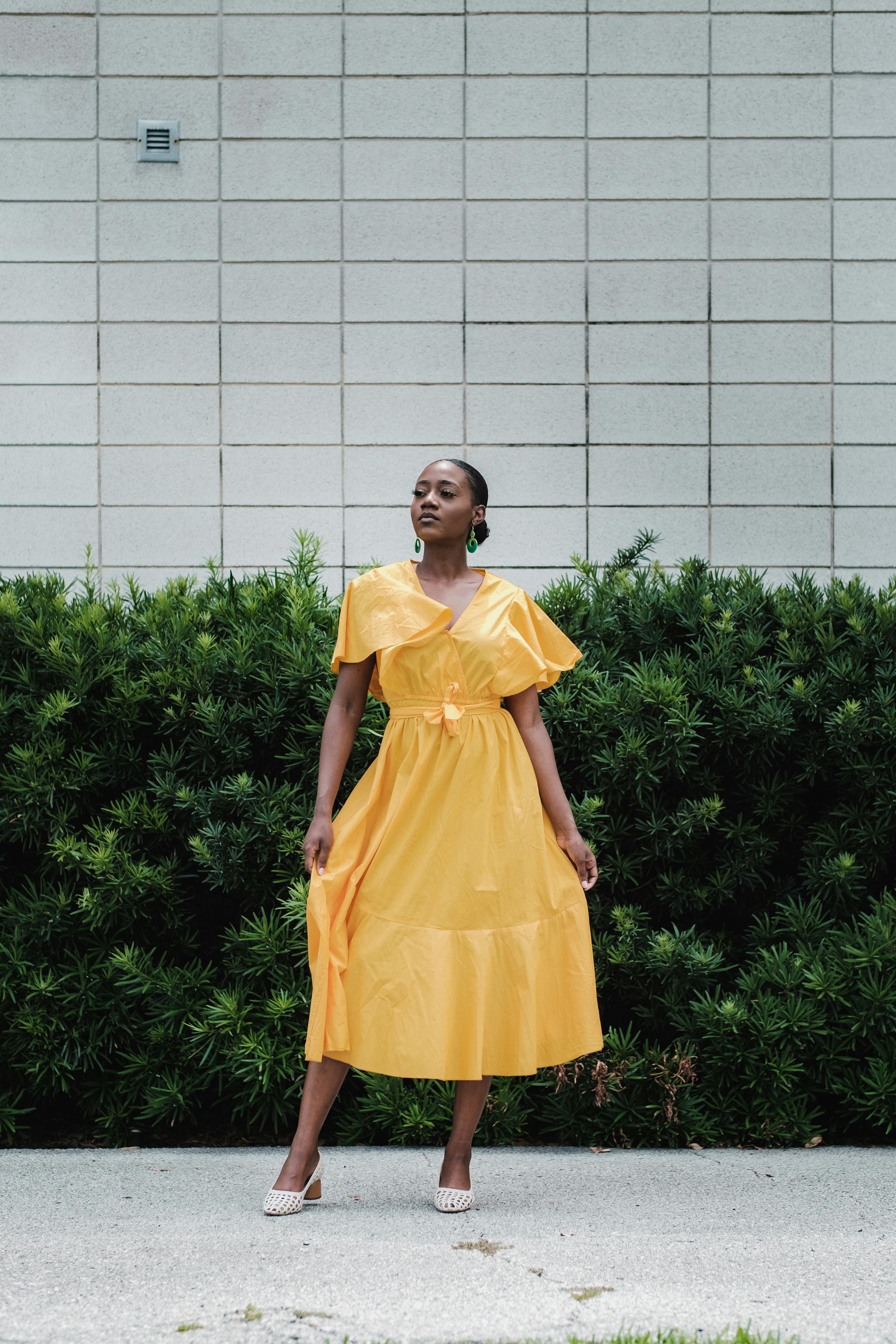 Stylish woman in a vibrant yellow dress posing confidently outdoors.
